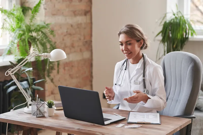 Smiling doctor speaking on her phone and writing notes at her desk